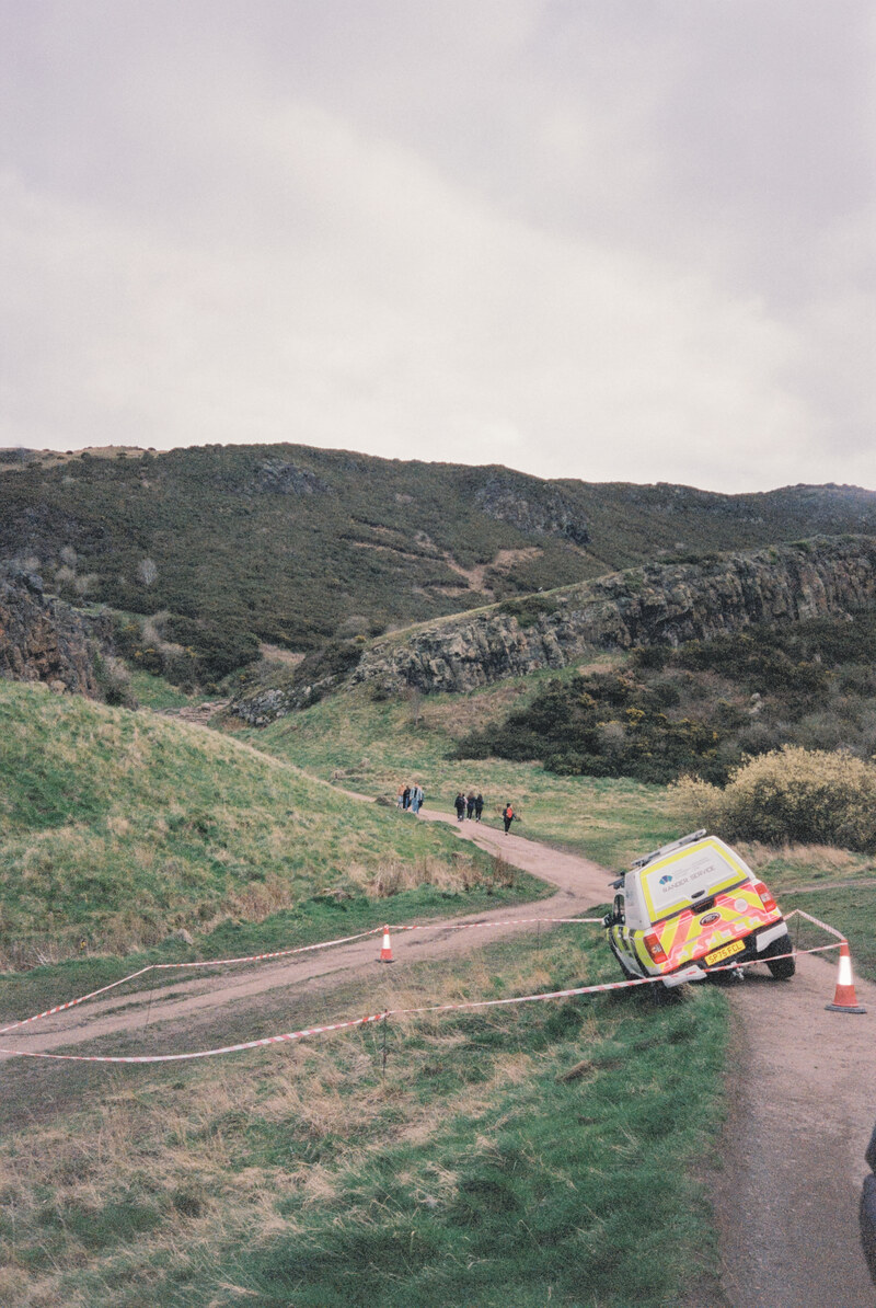 An ambulance on a road beneath rocky hills.