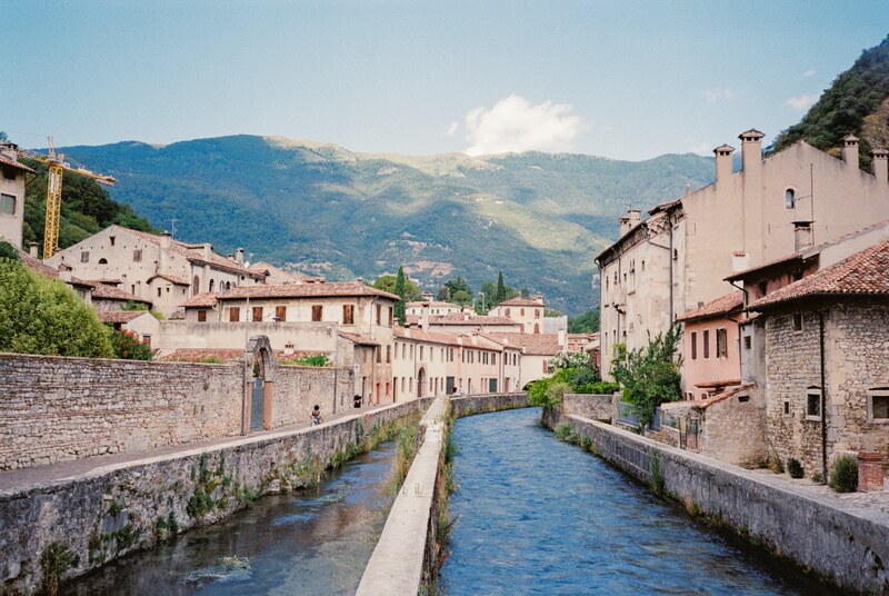 A river between old buildings in Serravalle, with mountains in the background.
